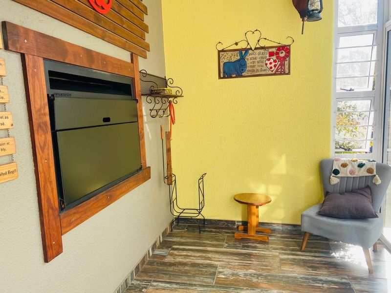 A cozy living area featuring a built-in Megamaster fireplace with a timber surround, wood-look tiled flooring, and a large window providing natural light.