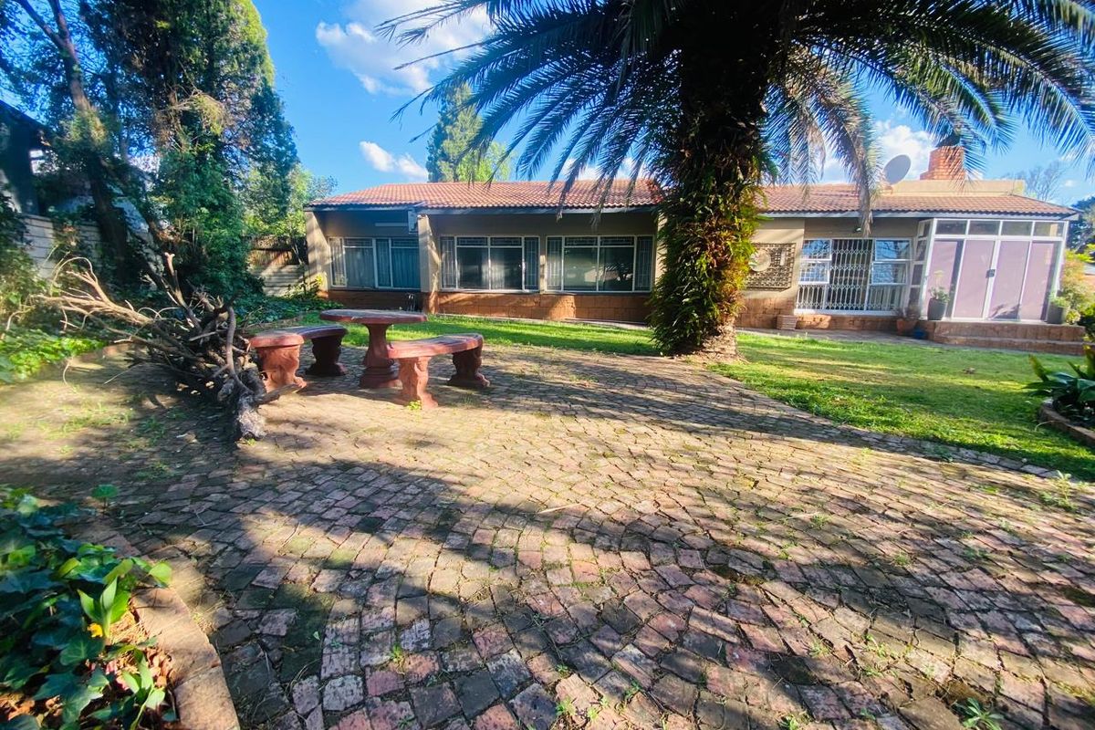 Rear view of the property featuring a brick-paved patio area, established garden, and a tiled roof structure.