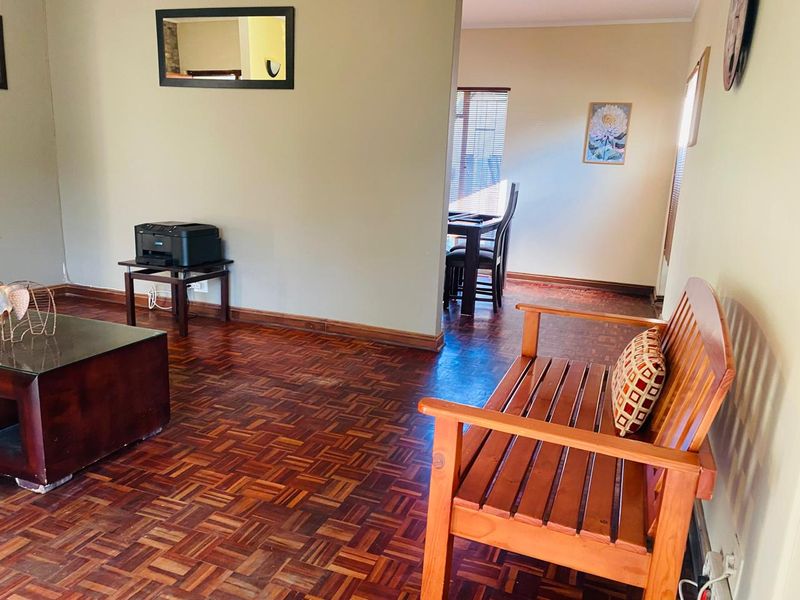 A living area featuring traditional parquet flooring and neutral wall finishes, with an open transition into the adjacent dining space.