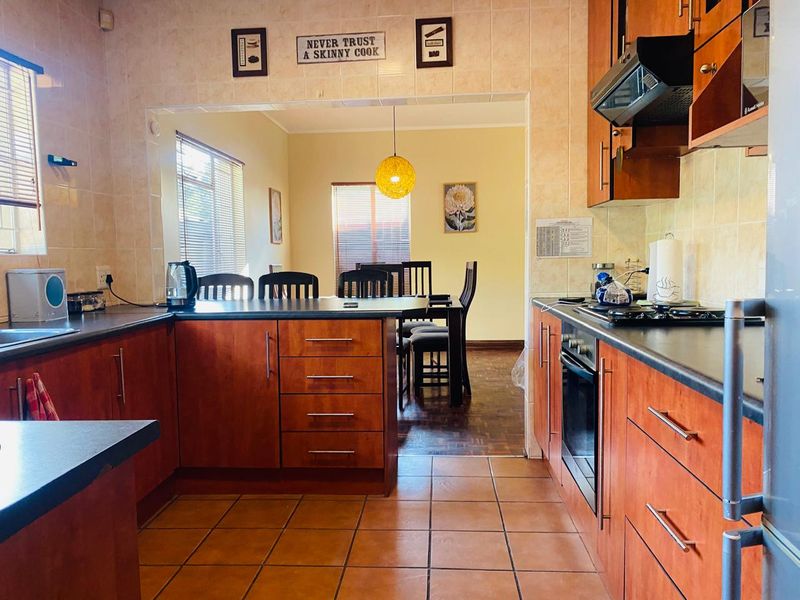 Open-plan kitchen featuring wooden cabinetry, dark countertops, and integrated appliances, flowing into a dining area with tiled flooring throughout.