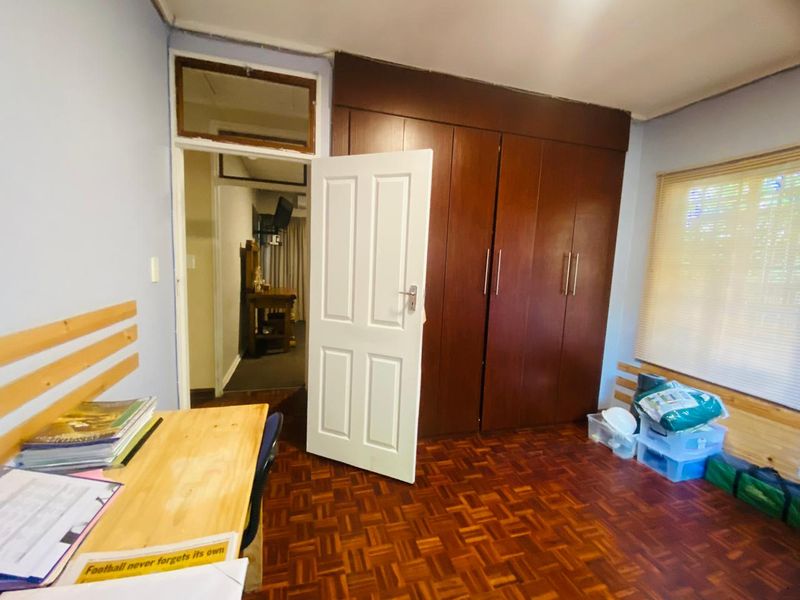 A bedroom featuring classic parquet flooring, built-in wooden cupboards, and a transom window above the doorway, offering a functional and traditional layout.