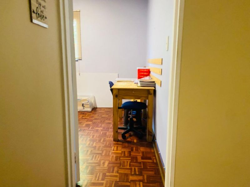 A small office space featuring classic parquet flooring and a window with fitted blinds, offering a functional area for work or study.