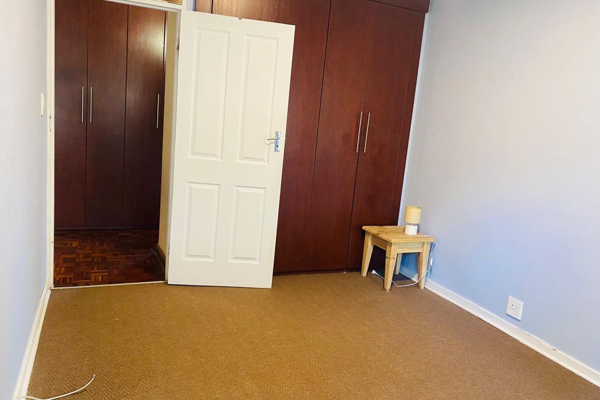 A bedroom featuring built-in wooden cupboards, a combination of carpet and parquet flooring, and a standard internal door.