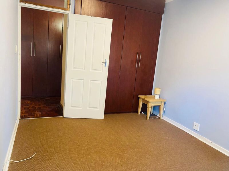A bedroom featuring built-in wooden cupboards, a combination of carpet and parquet flooring, and a standard internal door.