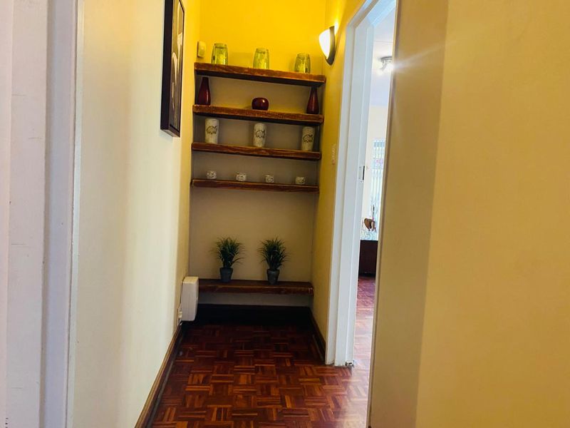 A narrow hallway featuring warm parquet flooring and built-in wooden shelving units, providing a functional transition space between rooms.