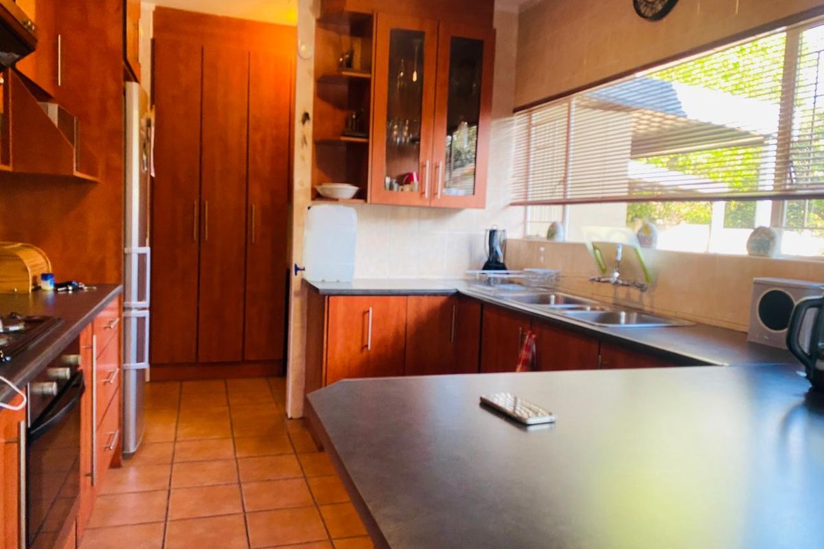 A functional kitchen featuring warm-toned wooden cabinetry, ample counter space, a double sink, and built-in cooking appliances with tiled flooring throughout.