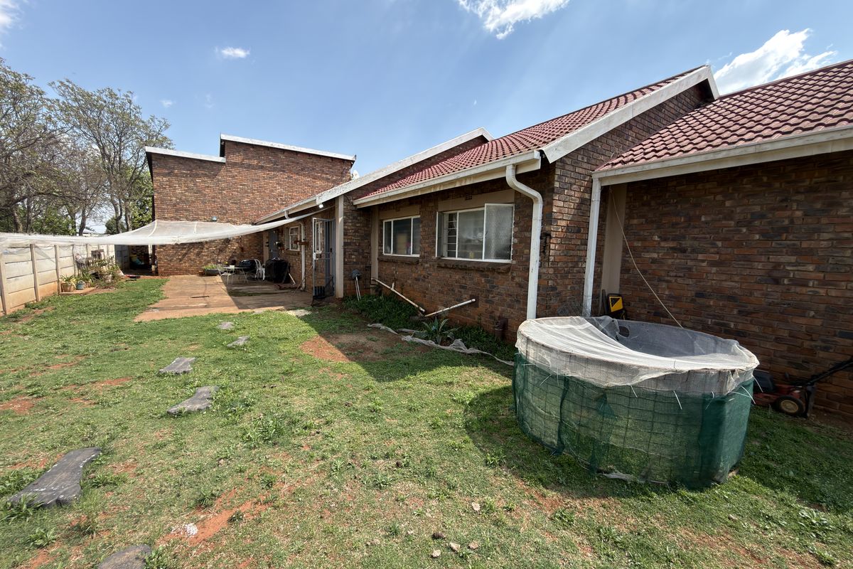 Rear view of the property featuring a brick facade, tiled roof, and a spacious backyard area with paved sections and established lawn.