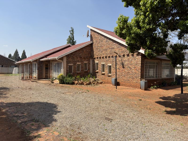 A single-story face brick house featuring a pitched tiled roof, security bars on windows, and an expansive unpaved driveway area.