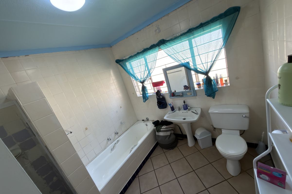 A functional bathroom featuring a bathtub, pedestal sink, and toilet, with tiled finishes and security bars on the window.