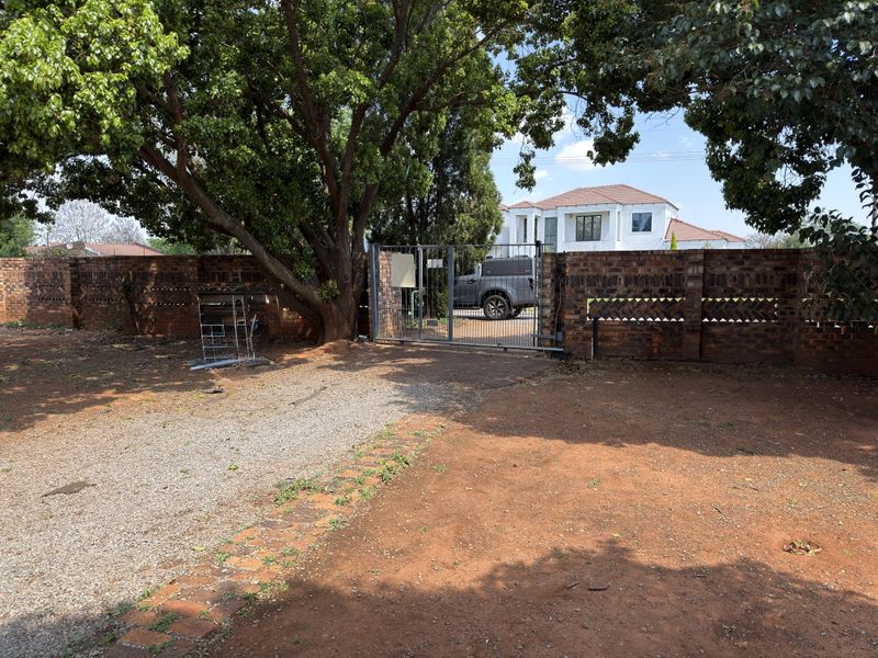 Front exterior view showing a gravel driveway, brick boundary wall, and metal security gate leading to the property entrance.