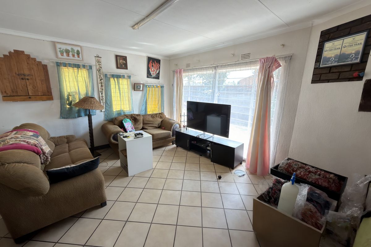 A living room featuring ceramic tile flooring, a large window with security bars, and a brick feature wall section.
