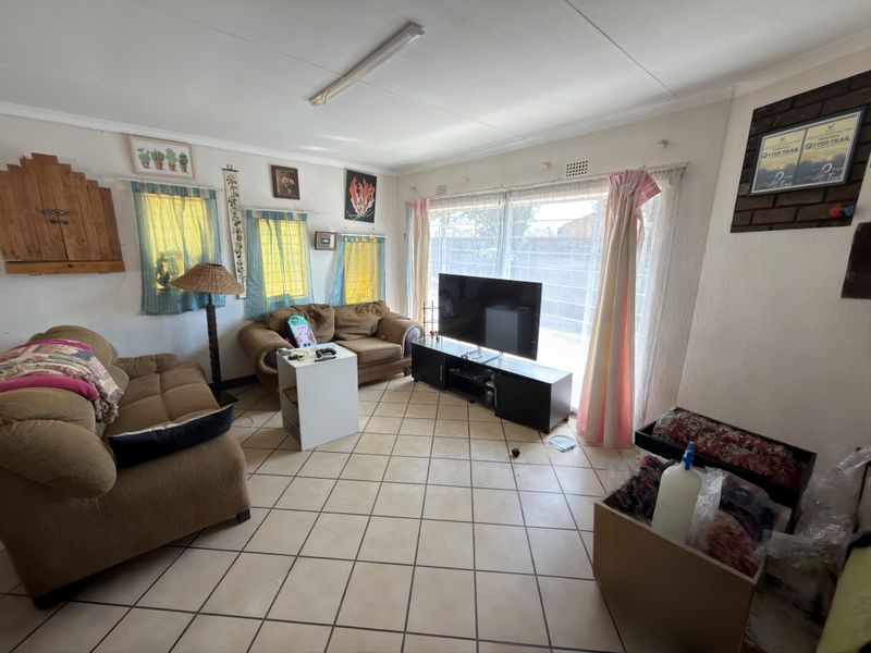 A living room featuring ceramic tile flooring, a large window with security bars, and a brick feature wall section.