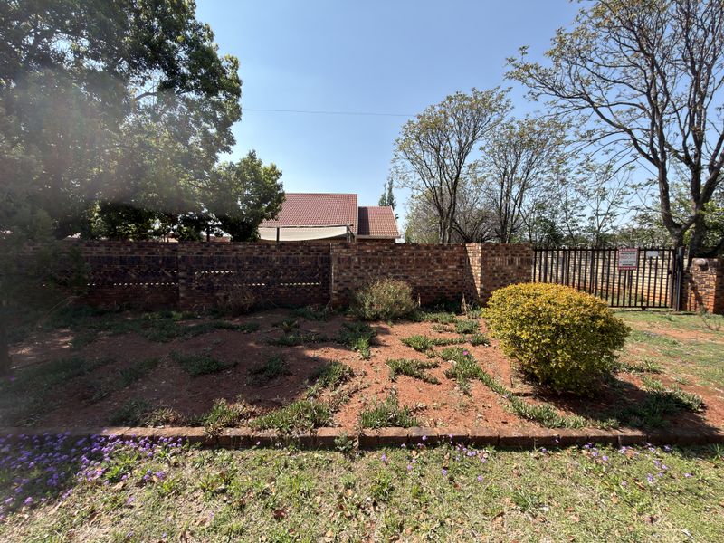 A view of the rear garden featuring a brick boundary wall, metal security gate, and established garden beds.