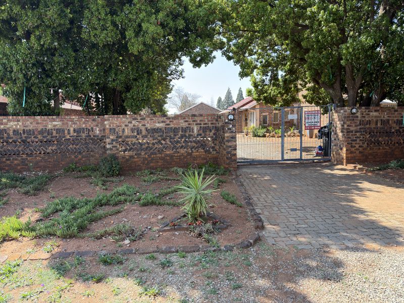 Front entrance view featuring a brick boundary wall, metal security gate, and paved driveway leading to the property.