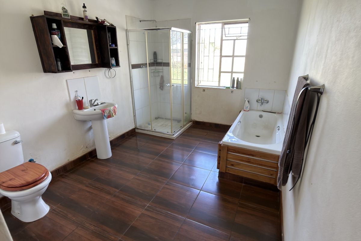 A spacious bathroom featuring a pedestal basin, separate shower enclosure, and a built-in bathtub with wood-look tiled flooring.