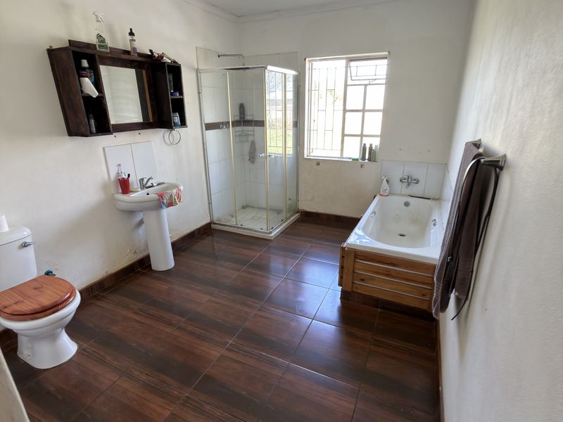 A spacious bathroom featuring a pedestal basin, separate shower enclosure, and a built-in bathtub with wood-look tiled flooring.