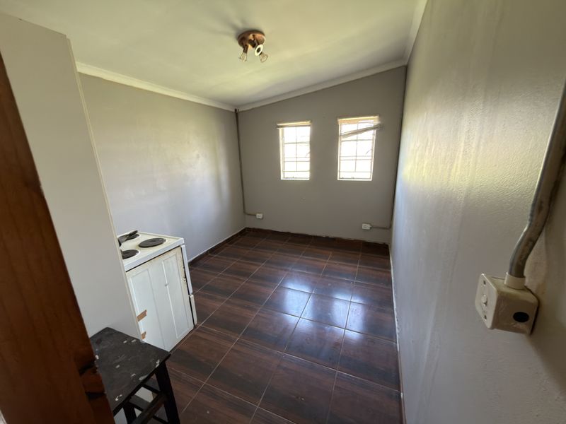 A compact, empty kitchen area featuring tiled flooring, a freestanding stove, and exposed electrical conduit, offering a blank canvas for renovation.