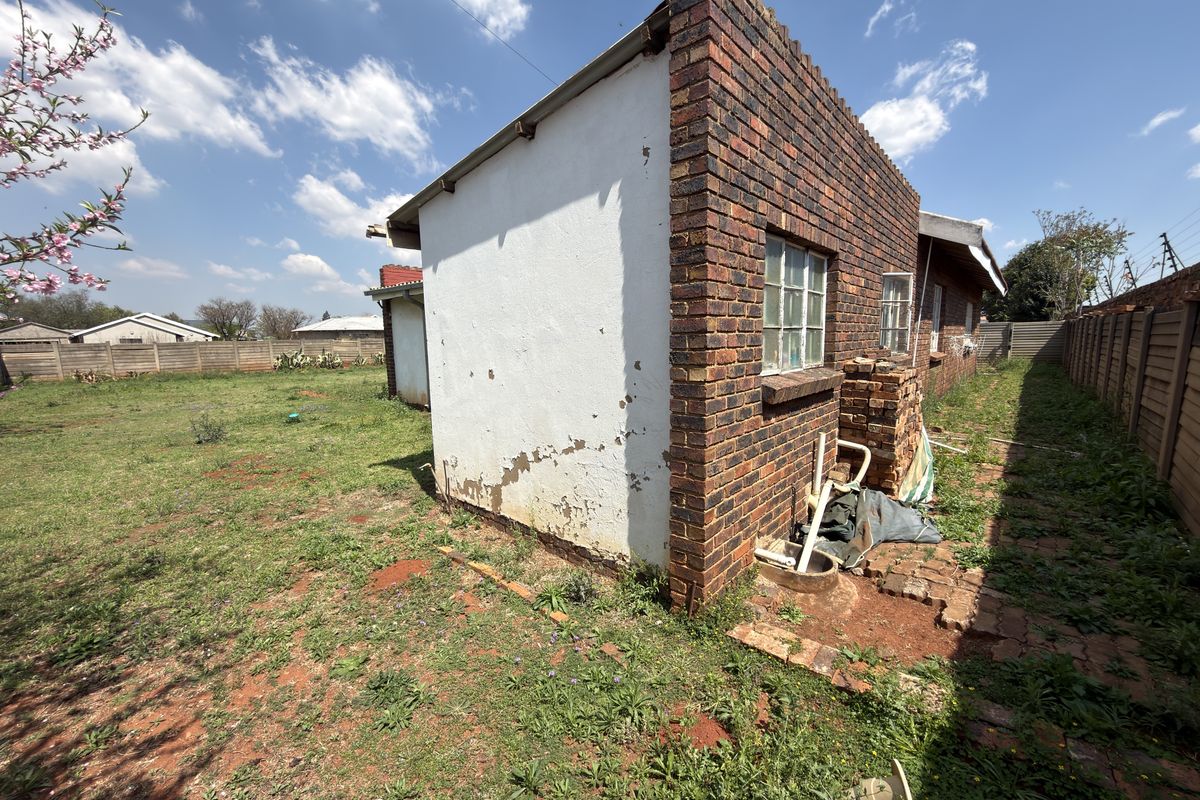 Rear view of the property showing brick exterior walls, steel window frames, and a large backyard enclosed by a precast concrete boundary wall.