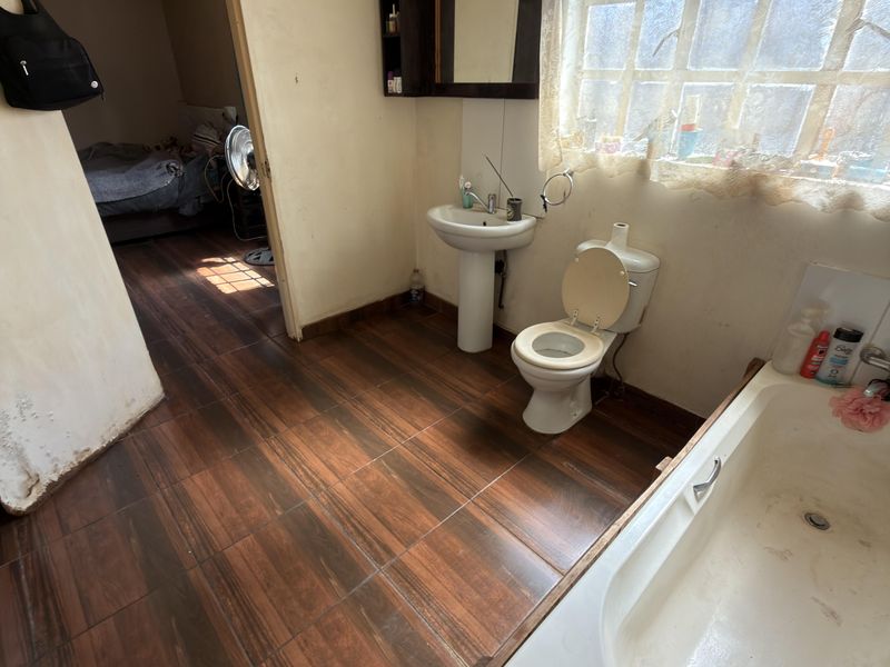 A dated bathroom featuring a pedestal basin, toilet, and bathtub with dark wood-look tiled flooring and natural light from a window.