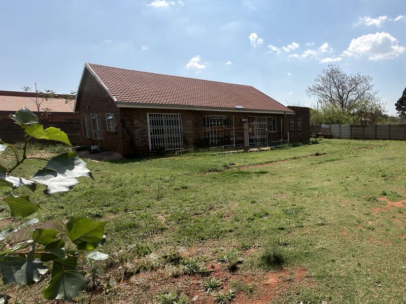 Rear view of a brick house featuring a tiled roof, security gates, and a large, open backyard area.