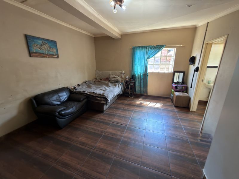A bedroom featuring dark wood-look floor tiles, a window with curtains, and direct access to an adjoining bathroom.