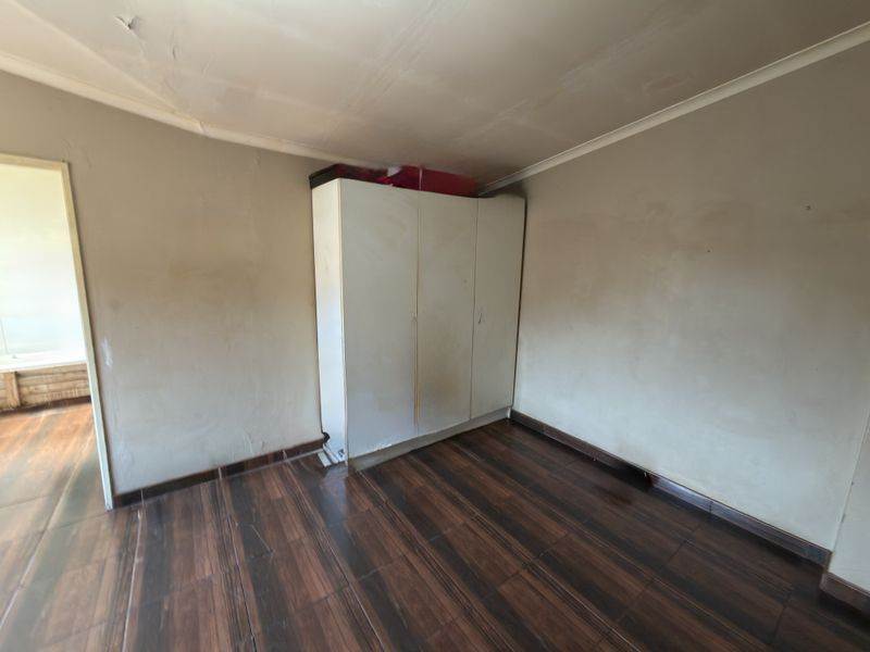 A vacant bedroom featuring dark tiled flooring, a built-in wardrobe, and visible signs of wear on the ceiling and walls.