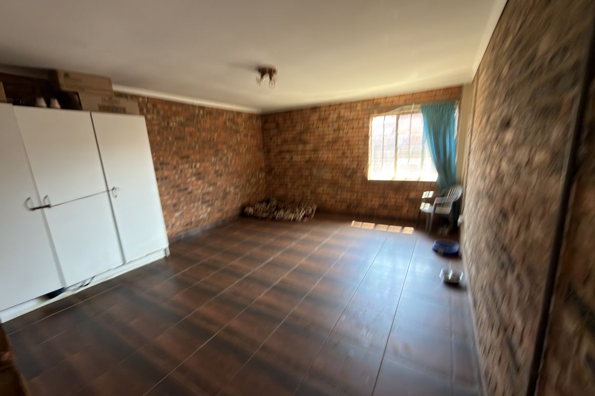 A spacious bedroom featuring exposed brick walls, dark tiled flooring, and a built-in wardrobe, offering a rustic aesthetic ready for personalization.