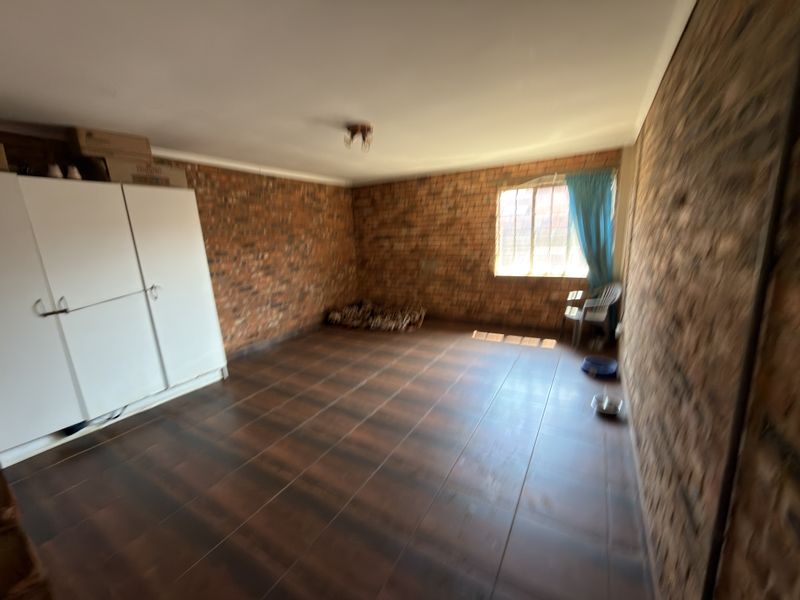 A spacious bedroom featuring exposed brick walls, dark tiled flooring, and a built-in wardrobe, offering a rustic aesthetic ready for personalization.