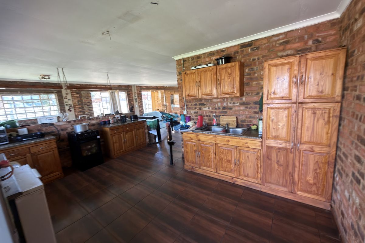 Spacious kitchen featuring exposed brick walls, wooden cabinetry, and tiled flooring, offering a rustic aesthetic with potential for modernization.
