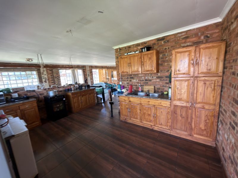 Spacious kitchen featuring exposed brick walls, wooden cabinetry, and tiled flooring, offering a rustic aesthetic with potential for modernization.