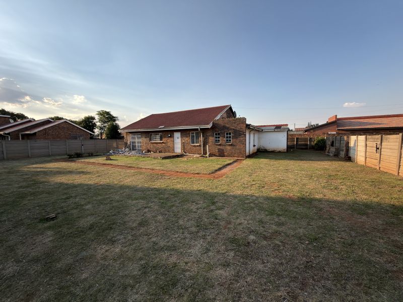 Rear view of a single-story brick house featuring a tiled roof, security bars on windows, and a large enclosed garden with boundary walls.