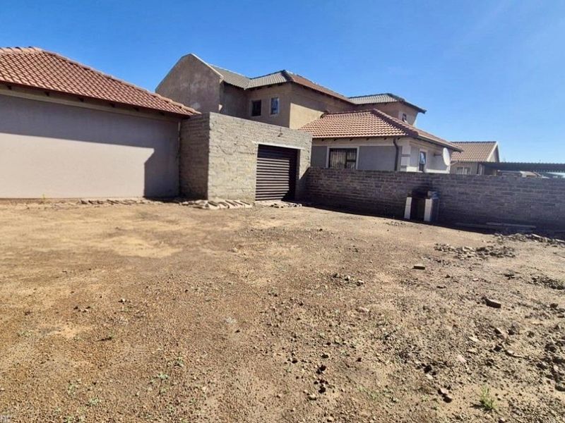 A spacious, unlandscaped rear yard featuring a brick boundary wall, tiled roof structures, and a private garage entrance.