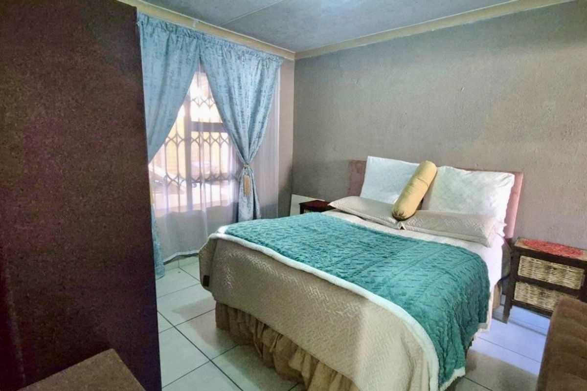 A bedroom featuring tiled flooring and a window with security gate, requiring cosmetic updates to the walls and ceiling to improve overall appeal.