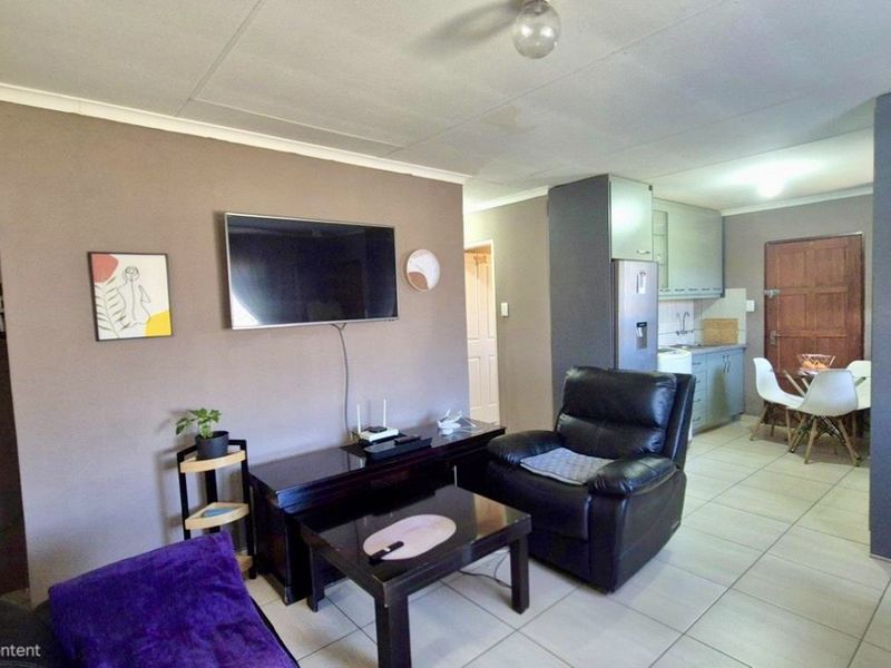 Open-plan living area featuring tiled flooring and a connected kitchen space with built-in cabinetry.