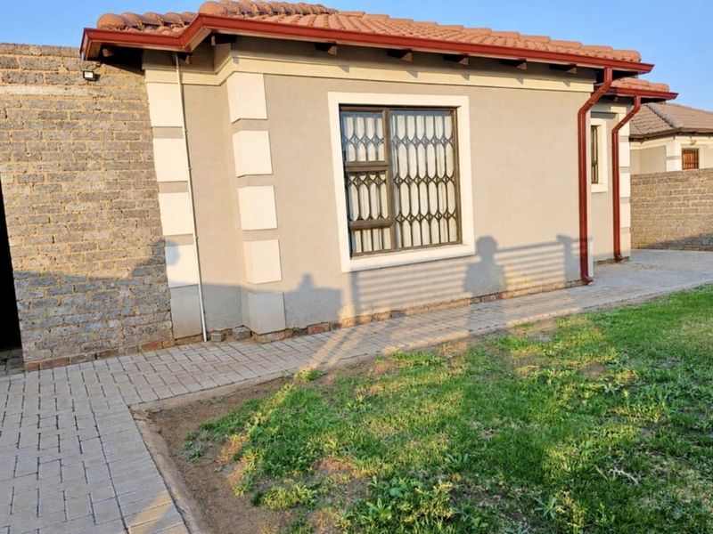 A view of the rear exterior of the house featuring a paved walkway, plastered walls, and a secure window with a metal gate.