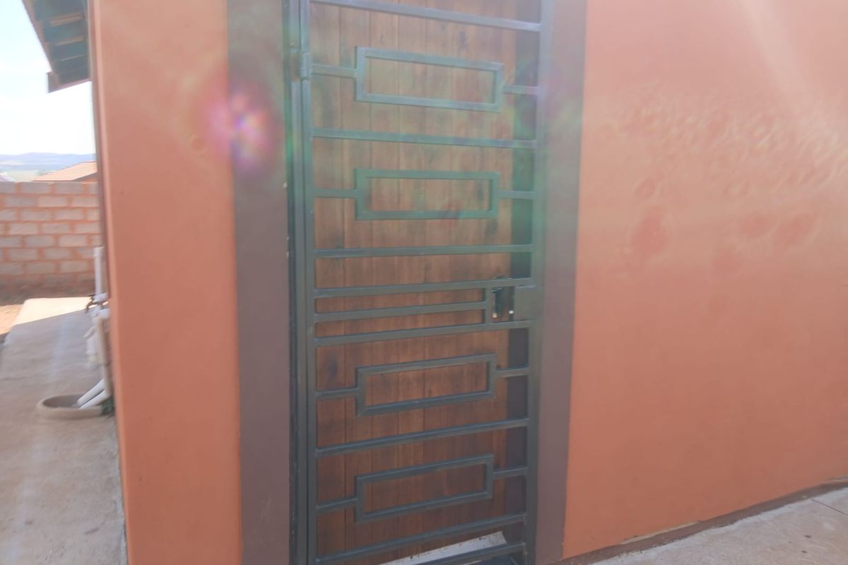 A rear exterior view showing a timber door protected by a dark metal security gate set into a plastered wall.