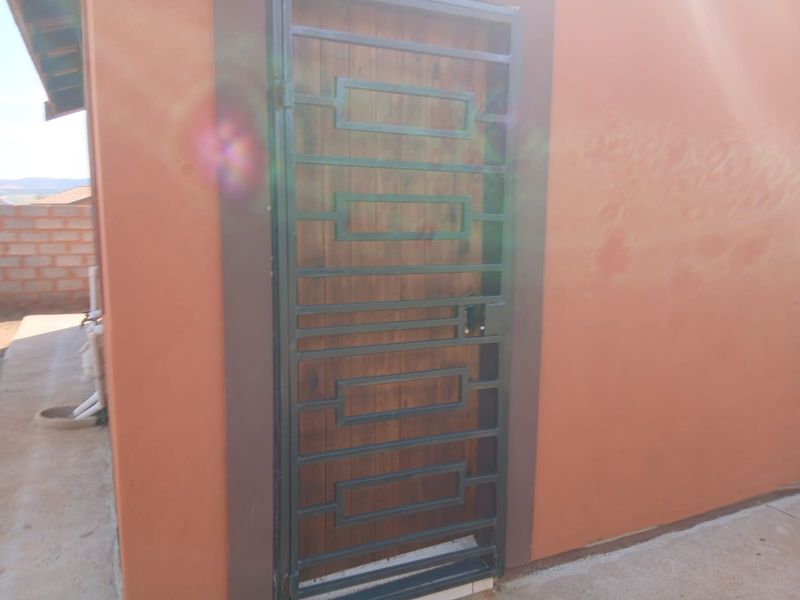 A rear exterior view showing a timber door protected by a dark metal security gate set into a plastered wall.