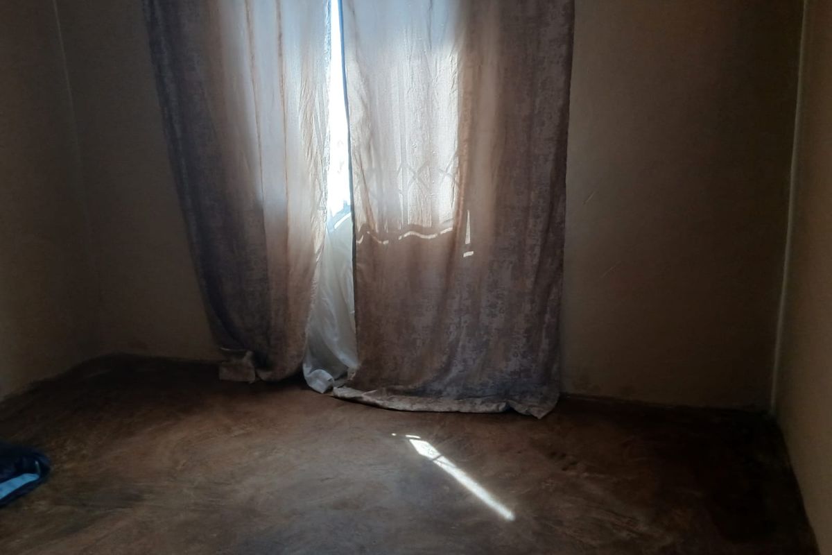An empty bedroom featuring a security gate and worn flooring, requiring cosmetic updates to improve its overall condition and appeal.
