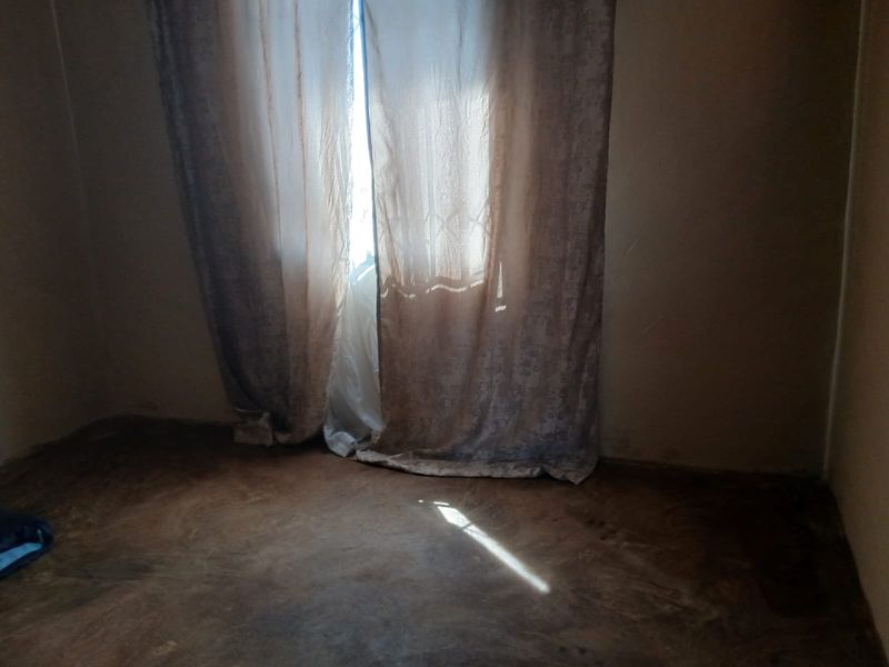 An empty bedroom featuring a security gate and worn flooring, requiring cosmetic updates to improve its overall condition and appeal.
