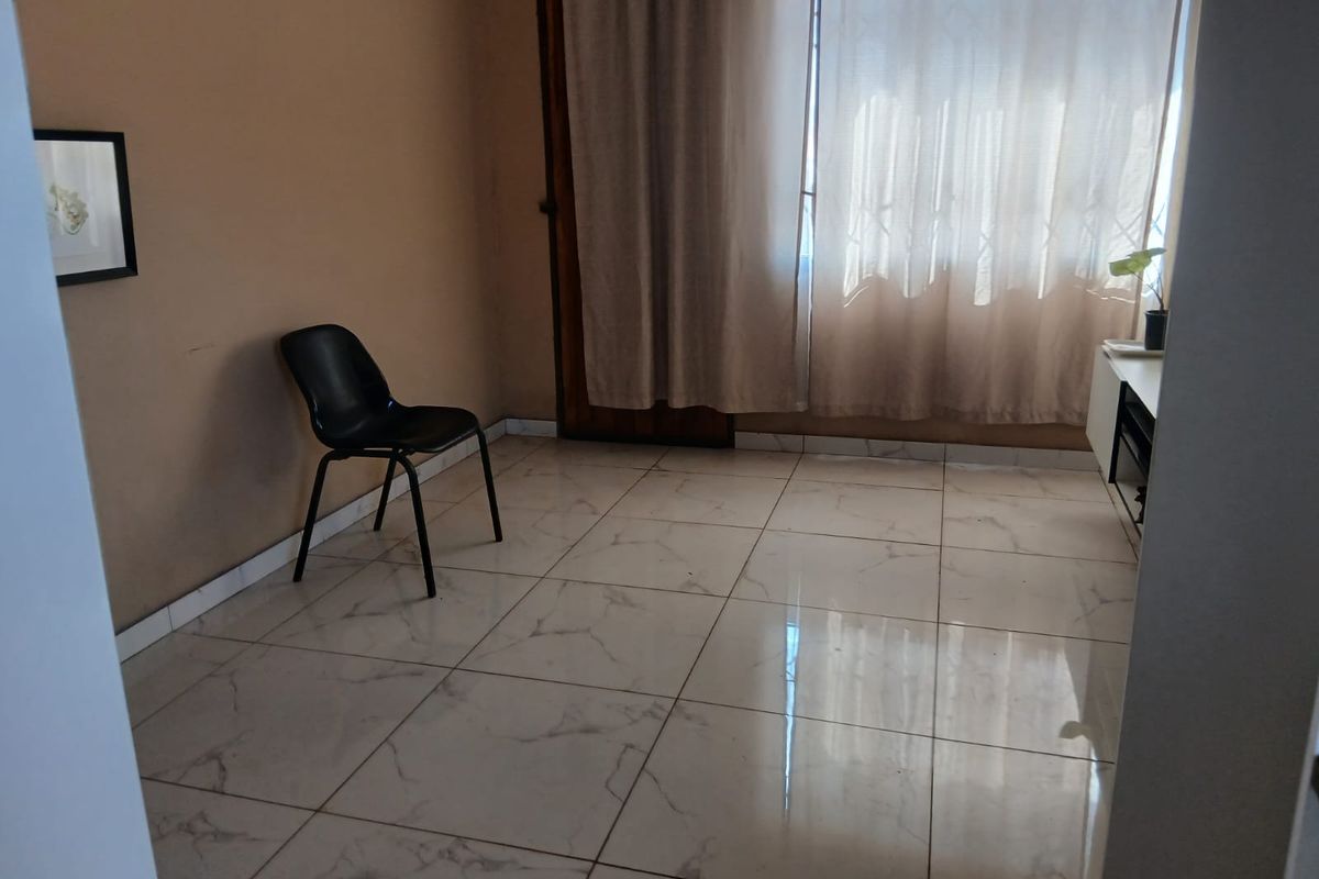 A bright, sparsely furnished living area featuring modern marble-look floor tiles and a large window with curtains.
