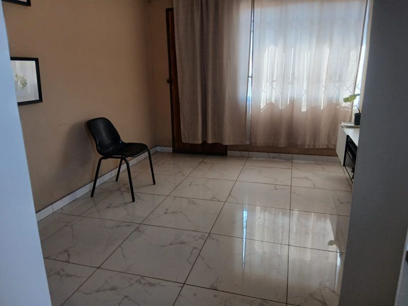 A bright, sparsely furnished living area featuring modern marble-look floor tiles and a large window with curtains.
