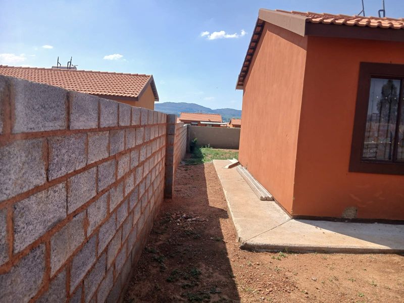Side exterior view of the property featuring a concrete block boundary wall, concrete pathway, and unfinished garden area.