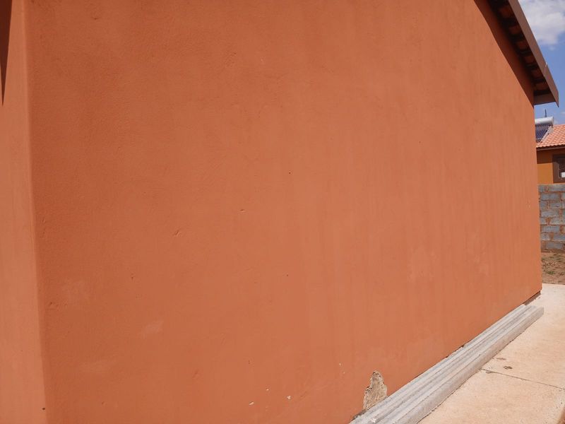 A view of the exterior rear wall showing the plastered finish and concrete plinth with minor plaster damage at the base.