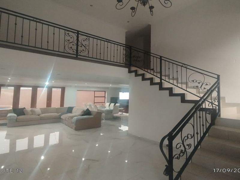 Spacious open-plan living area featuring a prominent staircase with decorative wrought iron railings and polished tiled flooring throughout.