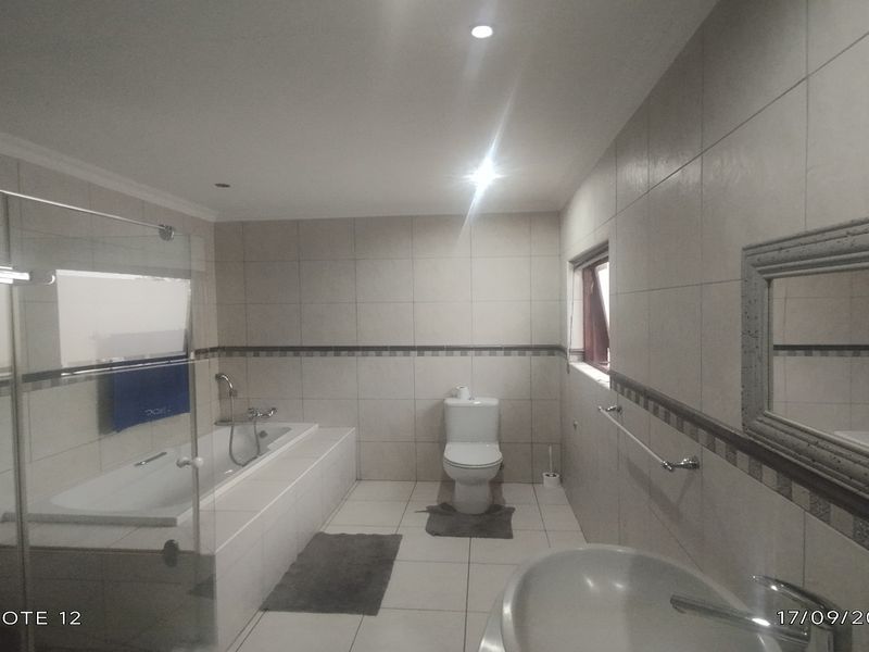 A spacious, tiled bathroom featuring a built-in bathtub, a separate glass-enclosed shower, a toilet, and a wall-mounted basin with a large mirror.