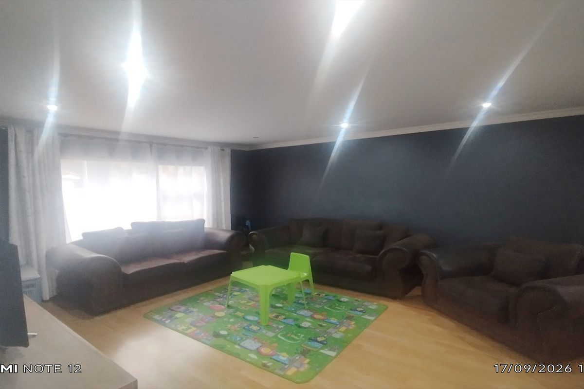 A spacious living room featuring laminate flooring, recessed downlighting, and a dark feature wall, providing a comfortable and versatile living space.
