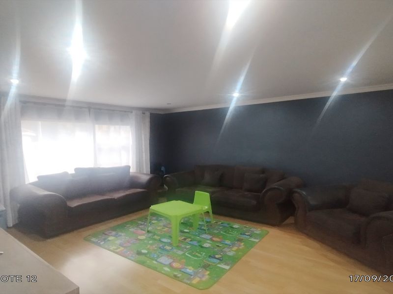 A spacious living room featuring laminate flooring, recessed downlighting, and a dark feature wall, providing a comfortable and versatile living space.