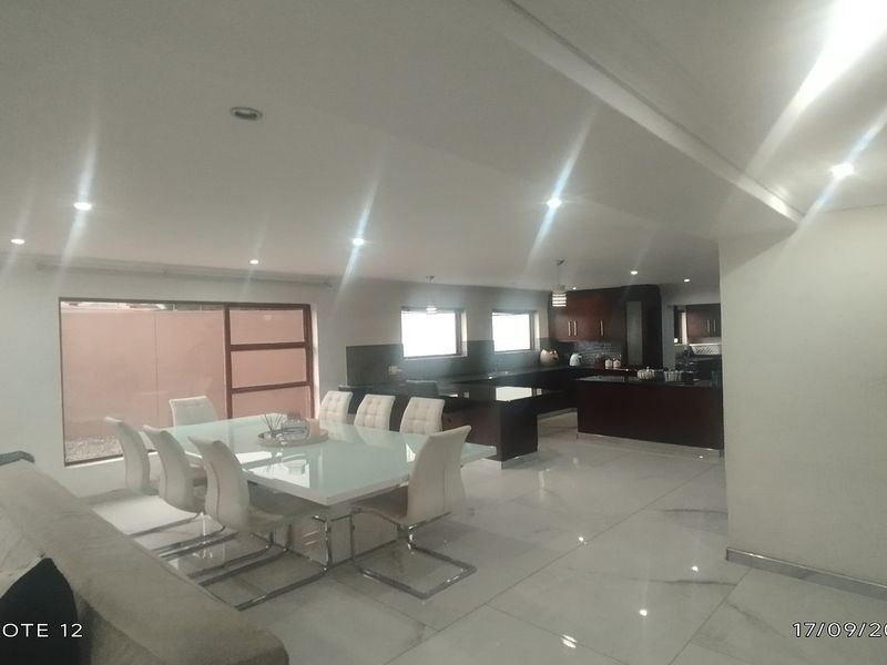 Spacious open-plan living and dining area featuring modern tiled floors, recessed lighting, and a functional kitchen with dark cabinetry.