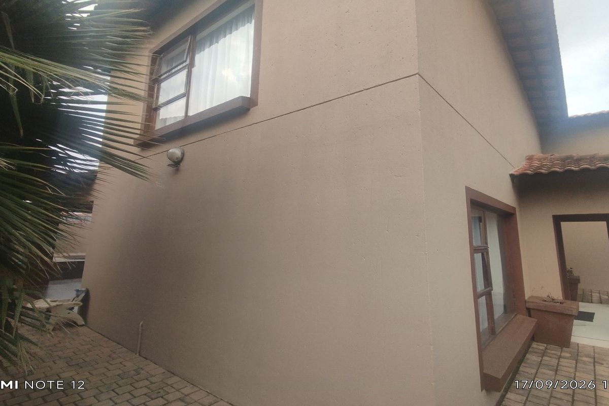 A view of the rear exterior of the townhouse featuring paved patio areas, tiled roofing, and aluminium window frames.