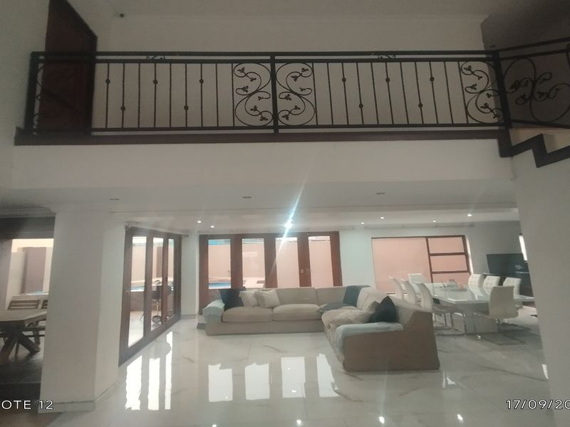 Spacious open-plan living and dining area featuring polished tiled floors, recessed lighting, and a decorative wrought iron staircase balustrade overlooking the ground floor.
